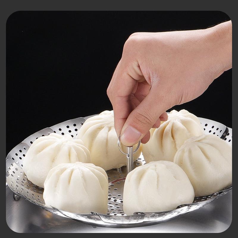 Hand using a steamer basket with buns on a black background